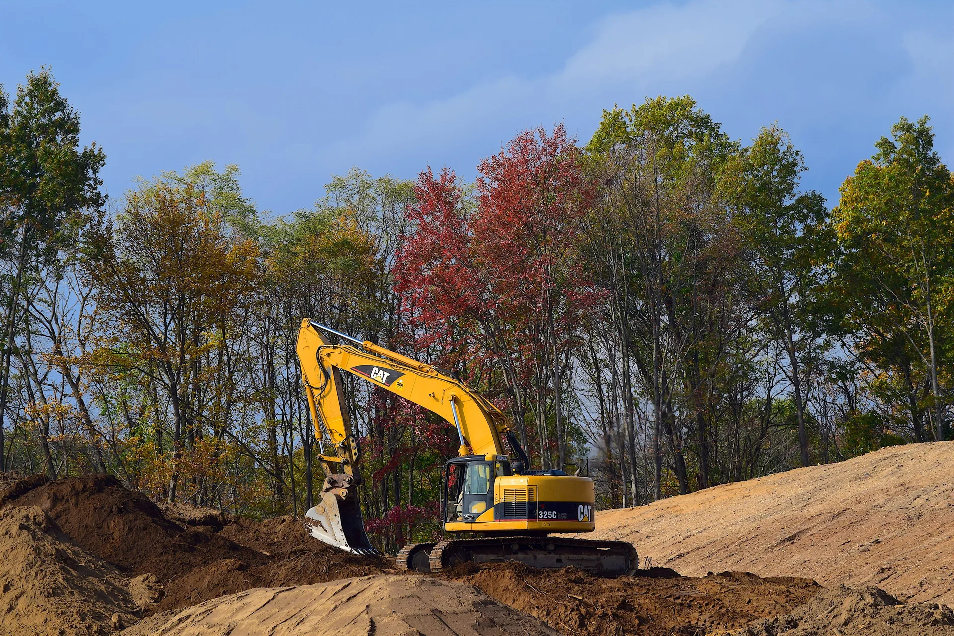 Excavator grading a cleared job site surrounded by fall foliage in Simcoe County